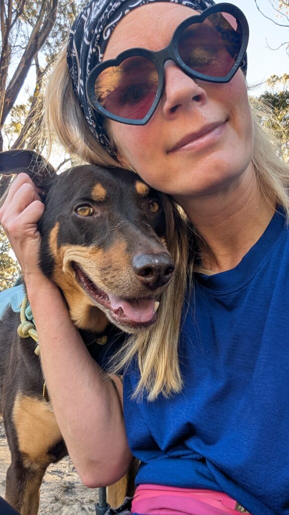 Woman wearing heart sunglasses hugging happy black and tan dog